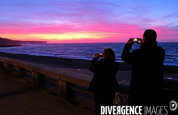 Un couple photographie le coucher de soleil sur la Manche et les falaises d  Etretat