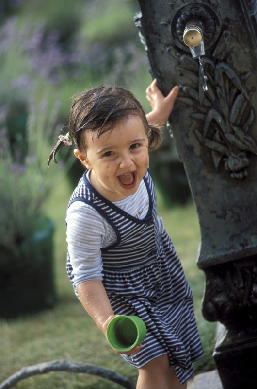 enfants, portraits Petite fille de 2 ans éclate de rire en jouant avec l'eau d'une fontaine. A little girl 2 years old laughs and plays with water of a fountain.