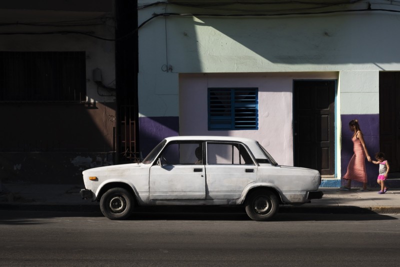 La lumière comme un couteau Une femme et une enfant passent sur le trottoir, une lada blanche est garée devant. 