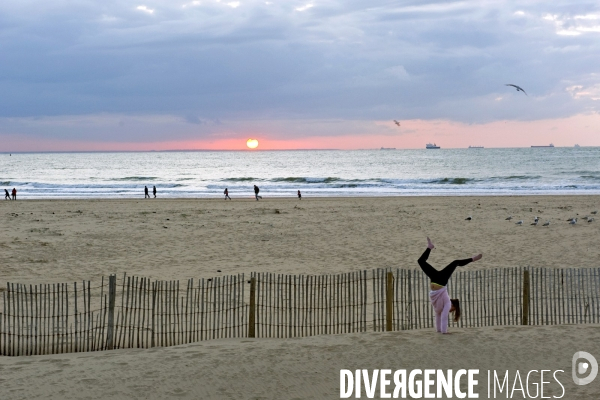 Mai 2016.Au coucher du soleil, une jeune fille fait une figure de gymnastique artistique  sur le sable