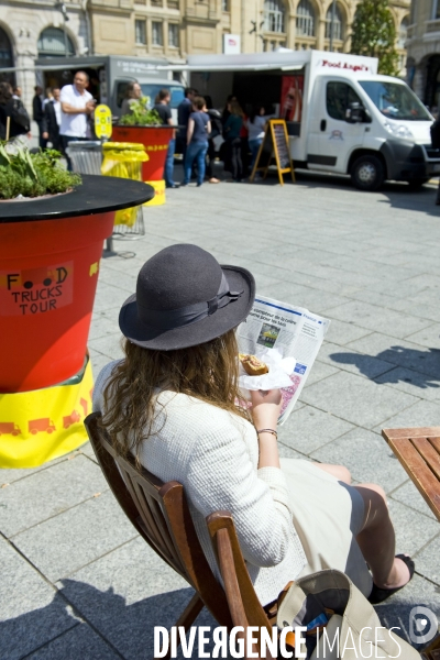 Illustration Juin 2014.Une jeune fille a la pause de midi, dejeune d un sandwich en lisant le journal 20 minutes.Food truk sur le parvis de la gare saint Lazare