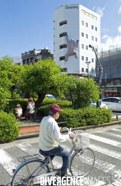 Japon. Tokushima.Un cycliste passe devant une sculpture de ratons laveurs et de King Kong escaladant la facade d un immeuble.